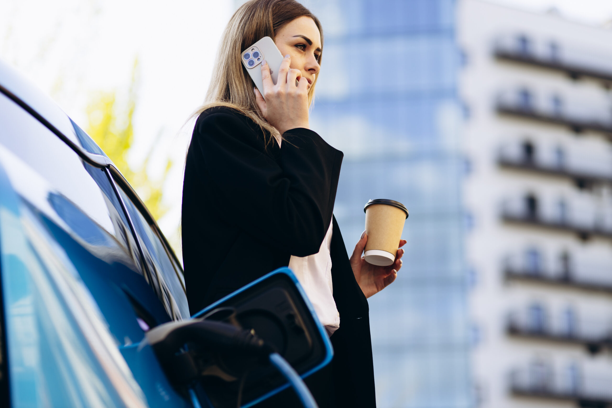 Businessfrau lehnt sich entspannt an ihr Elektroauto, das gerade aufgeladen wird.