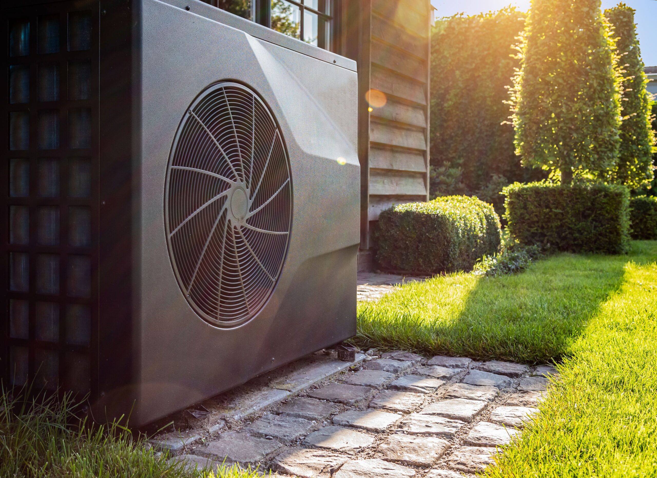 Eine Wärmepumpe steht im Garten vor einem Gartenhaus